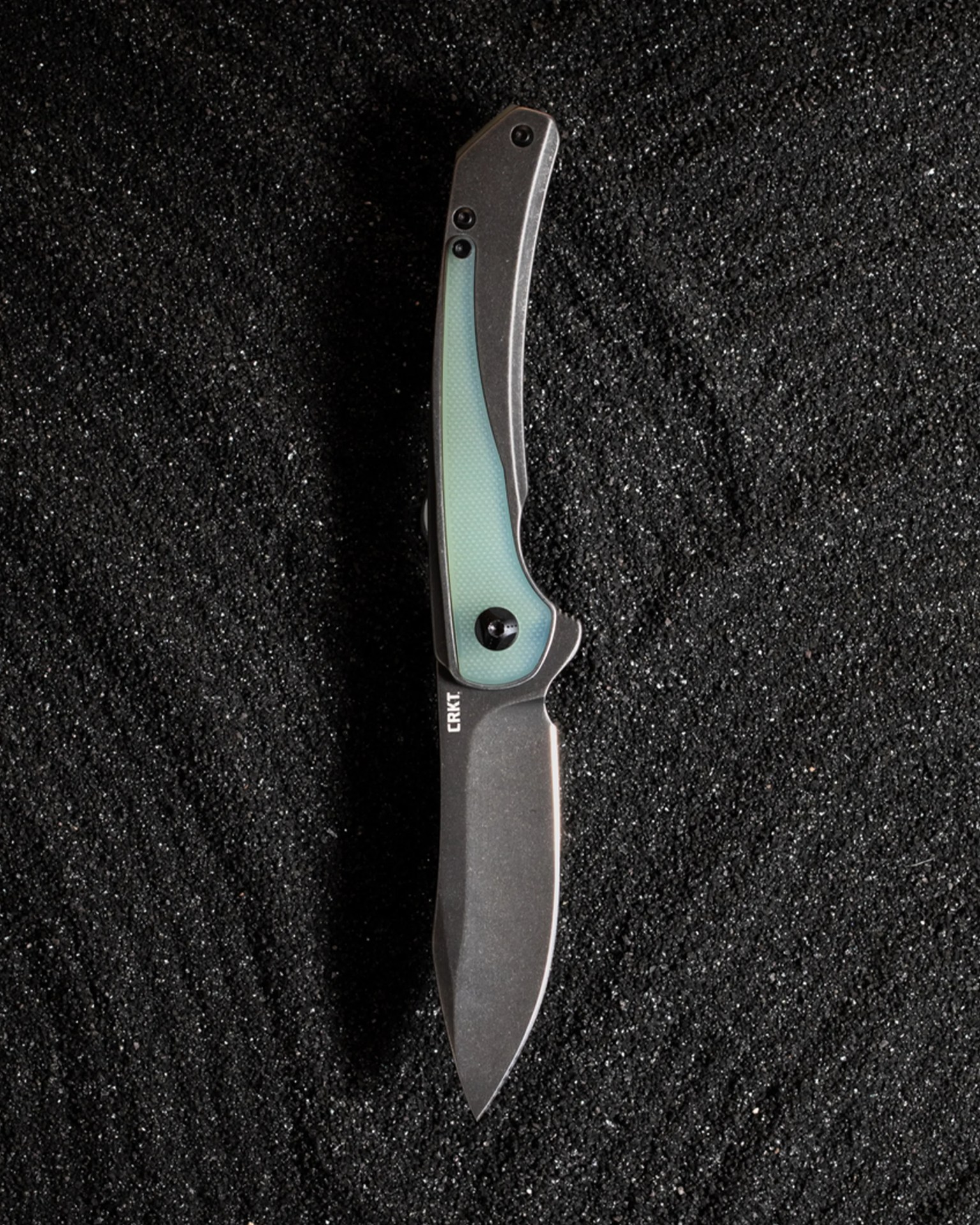 Folding knife with a dark stonewashed blade and a gray handle featuring a translucent green inlay, on black textured surface.