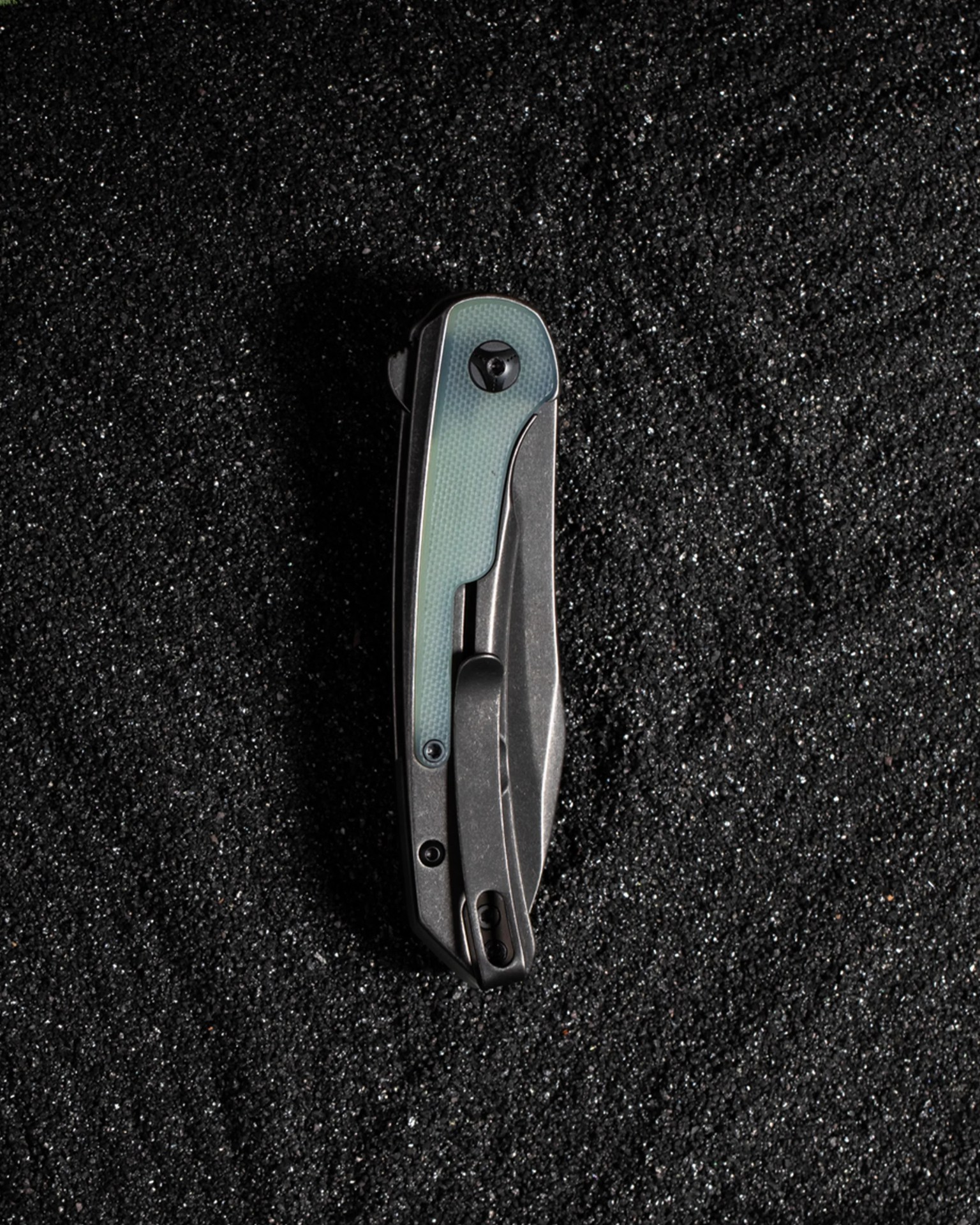 Folded black and gray pocket knife with a textured light blue handle panel on black granular surface.