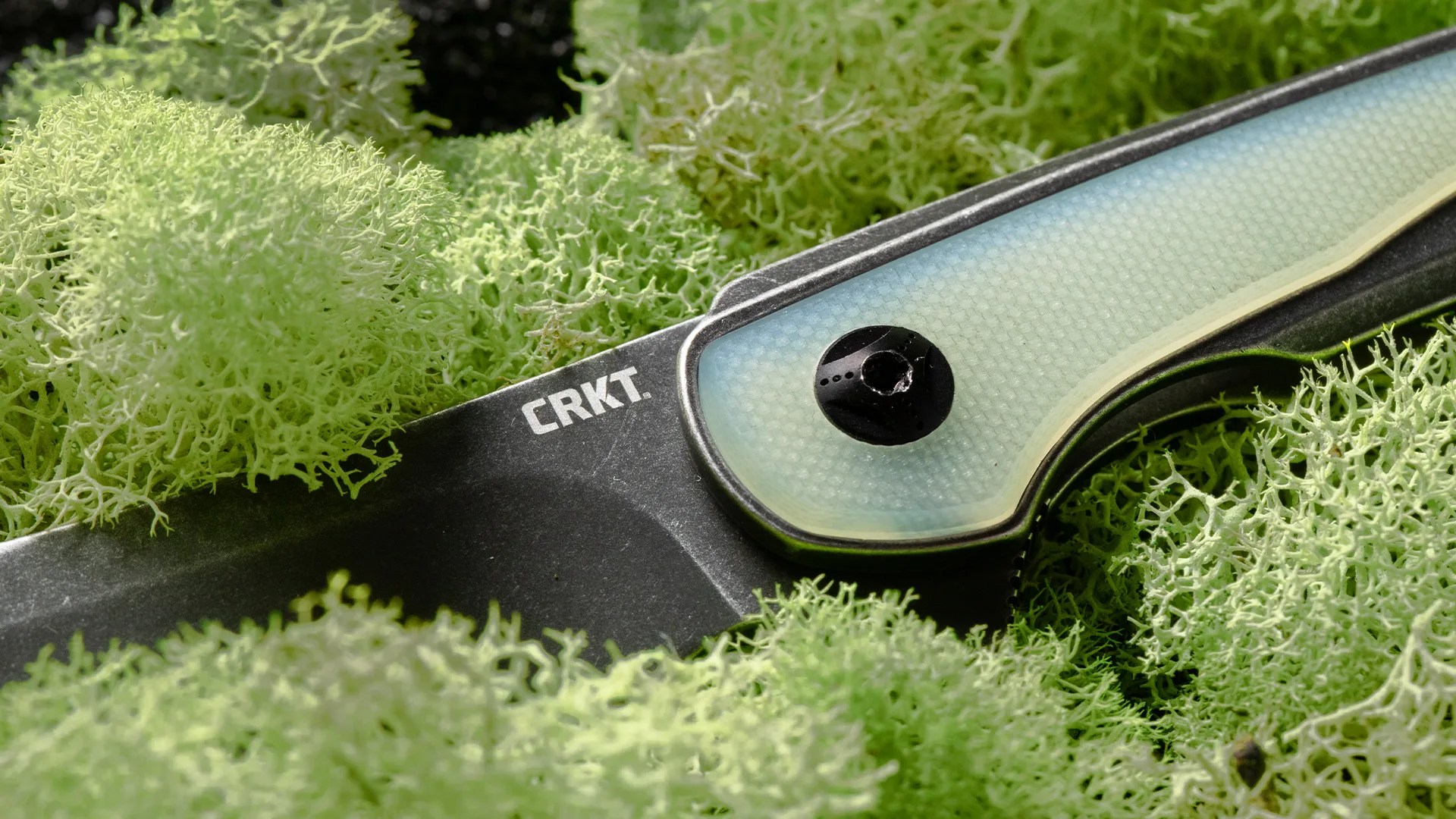 Close-up of a CRKT folding knife with a translucent blue handle resting on green moss.