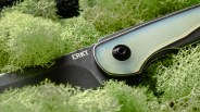 Close-up of a CRKT folding knife with a translucent blue handle resting on green moss.
