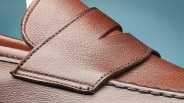 Close-up of brown leather shoe with detailed stitching and textured finish against a blue background.