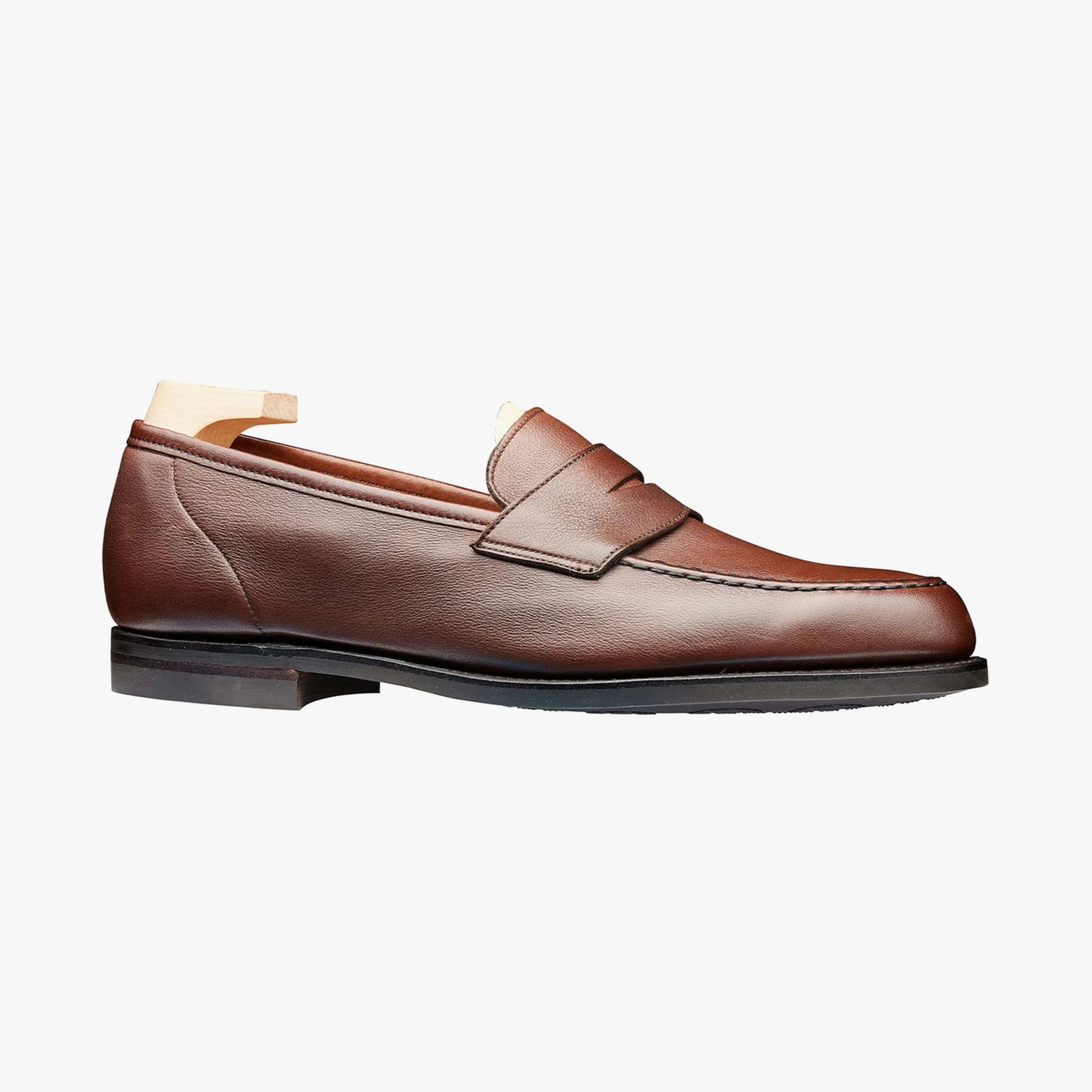 Brown leather penny loafer with black sole and wooden shoe tree inside.