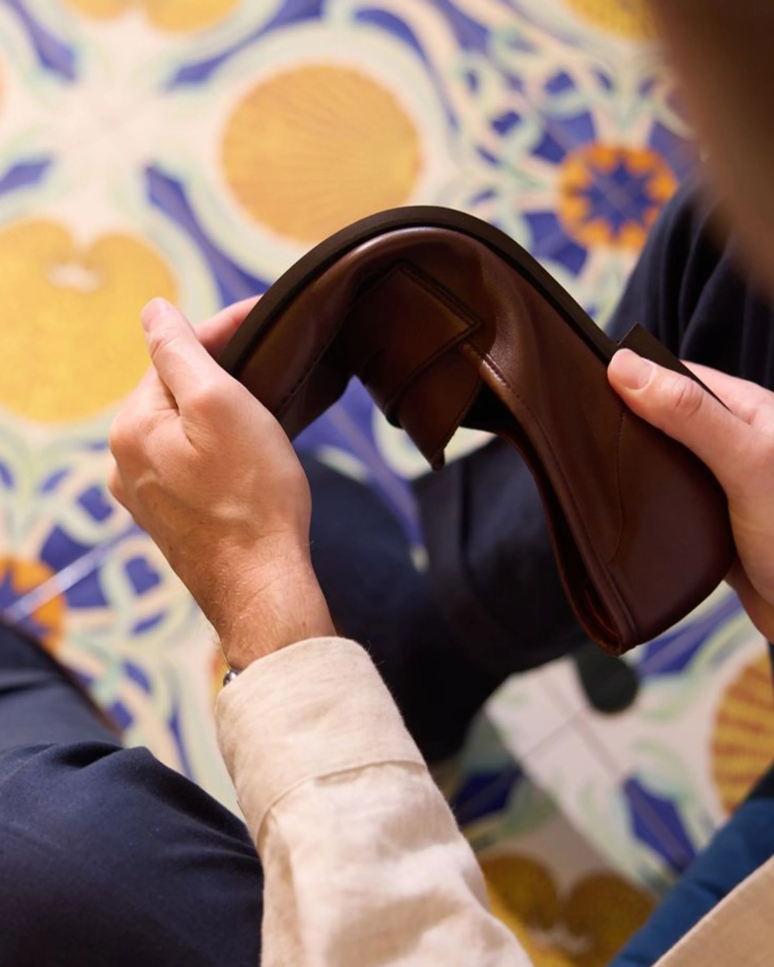 Person holding and bending a flexible brown leather shoe over patterned tile flooring.