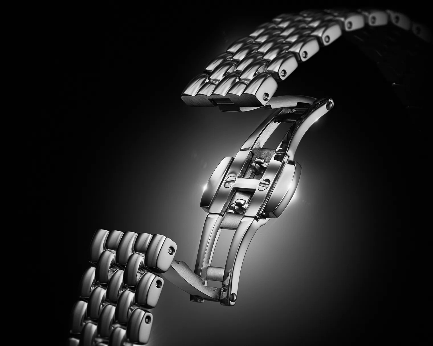 Polished stainless steel watch bracelet with a butterfly clasp open against a dark gradient background.
