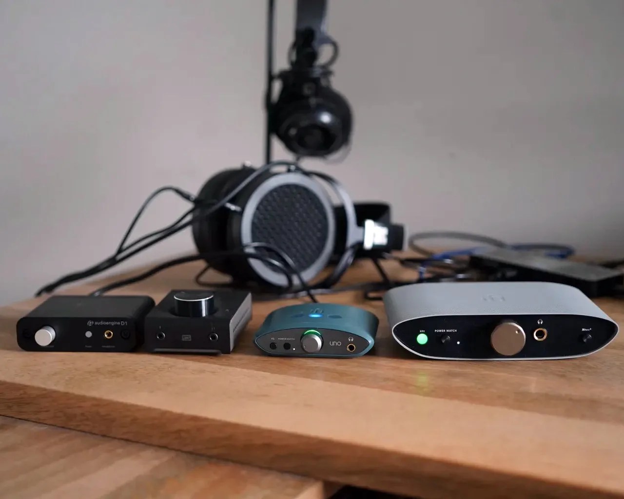 Four headphone amplifiers and a pair of headphones on a wooden surface with cables connected.