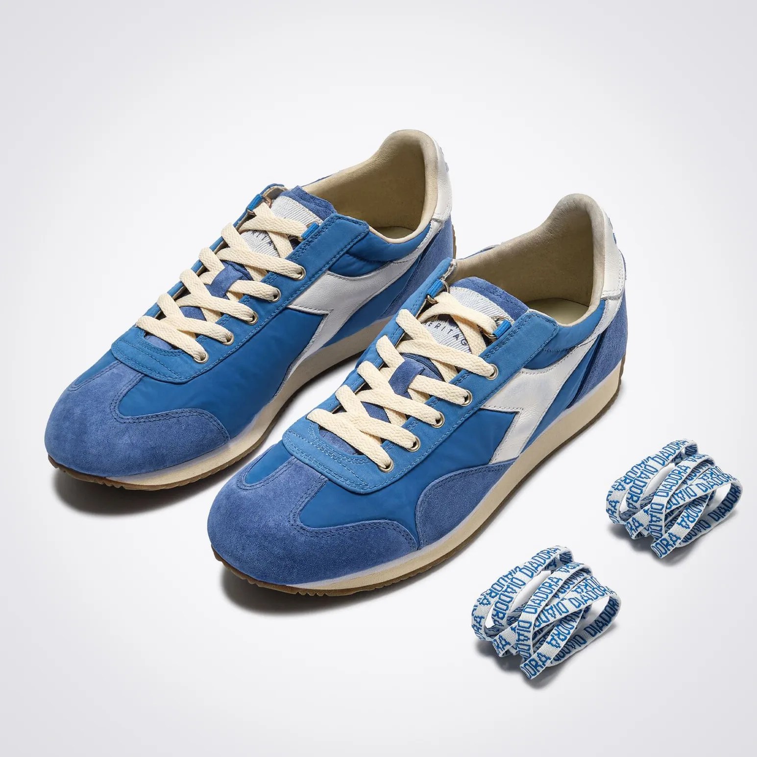 Pair of blue and white sneakers with cream laces and two extra sets of blue and white branded laces on a white background.