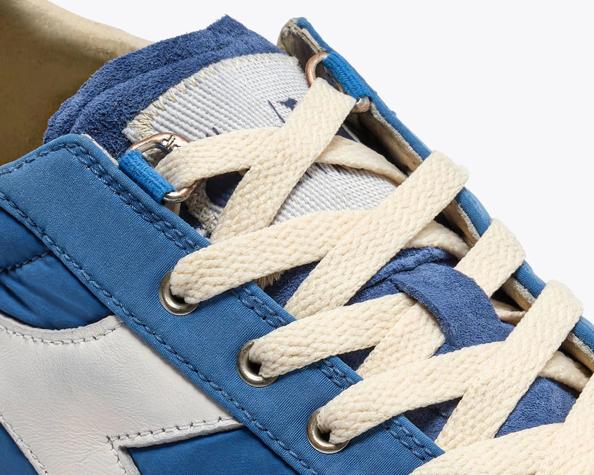 Close-up of blue and white sneaker with cream-colored woven laces threaded through metal eyelets.