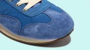 Close-up of a blue suede and fabric sneaker toe with beige laces on a light blue background.