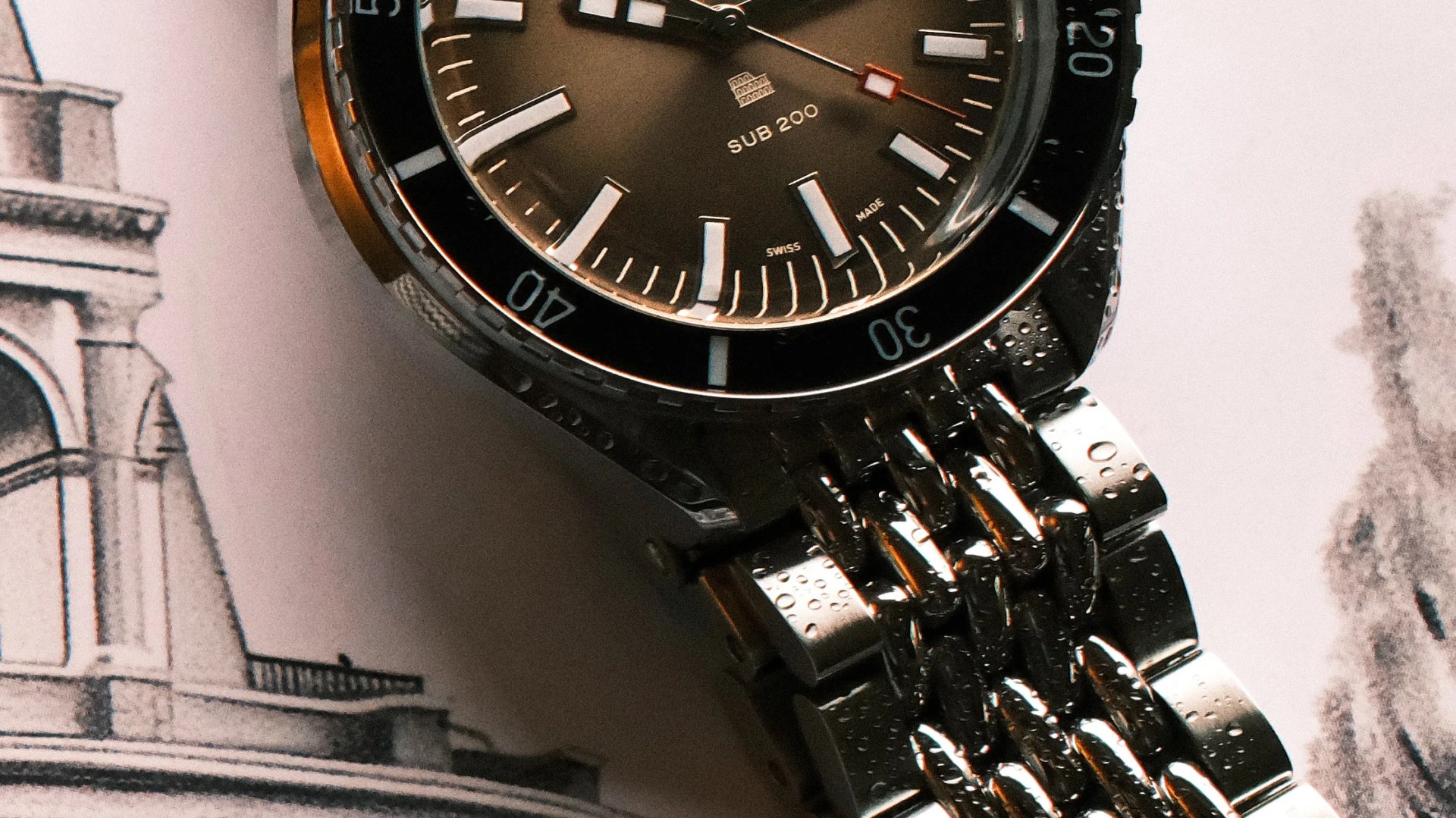 Close-up of a stainless steel wristwatch with a black bezel and water droplets on the bracelet.