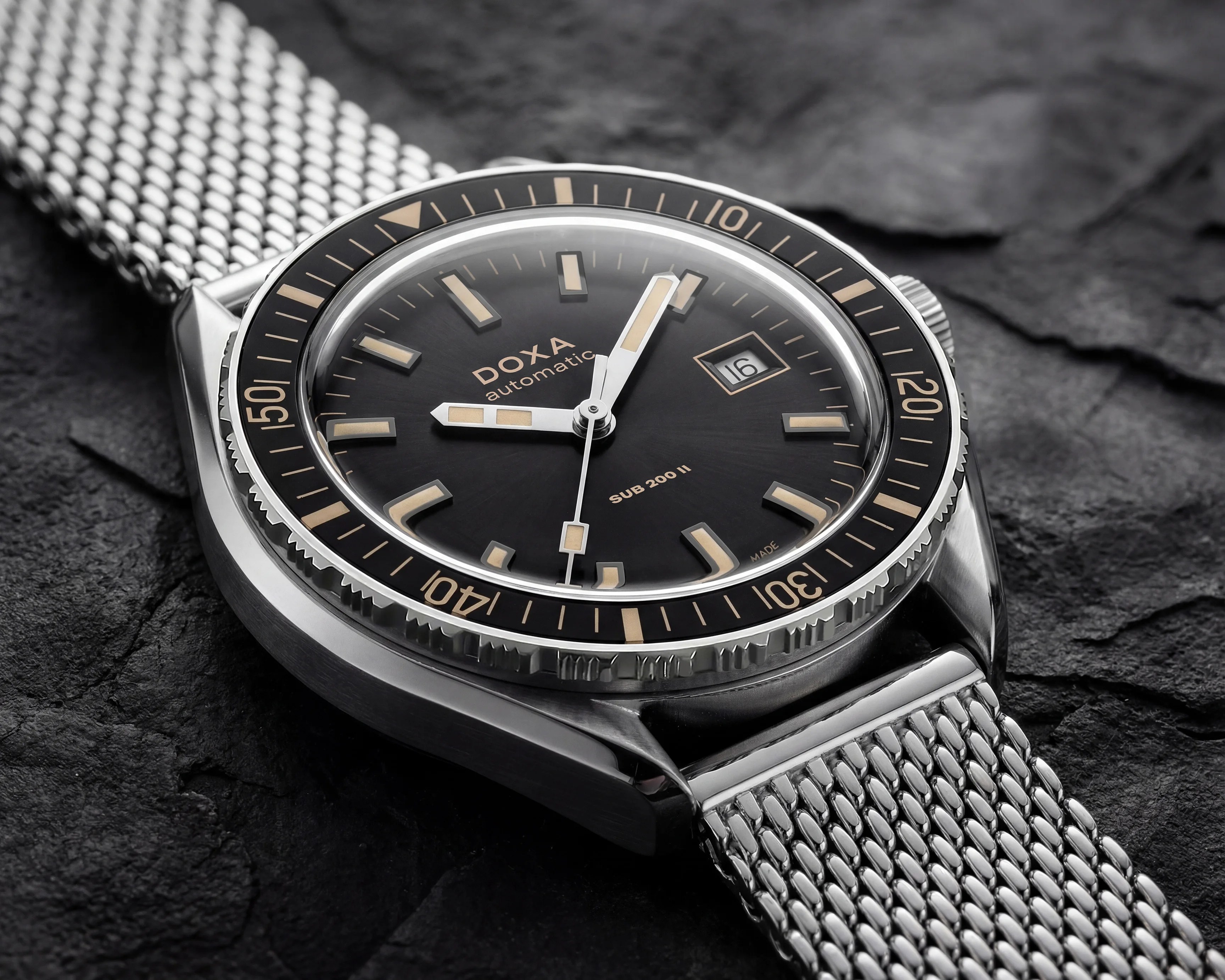 Stainless steel DOXA SUB 200 II automatic watch with black dial, beige markers, date window, and mesh bracelet on dark textured surface.