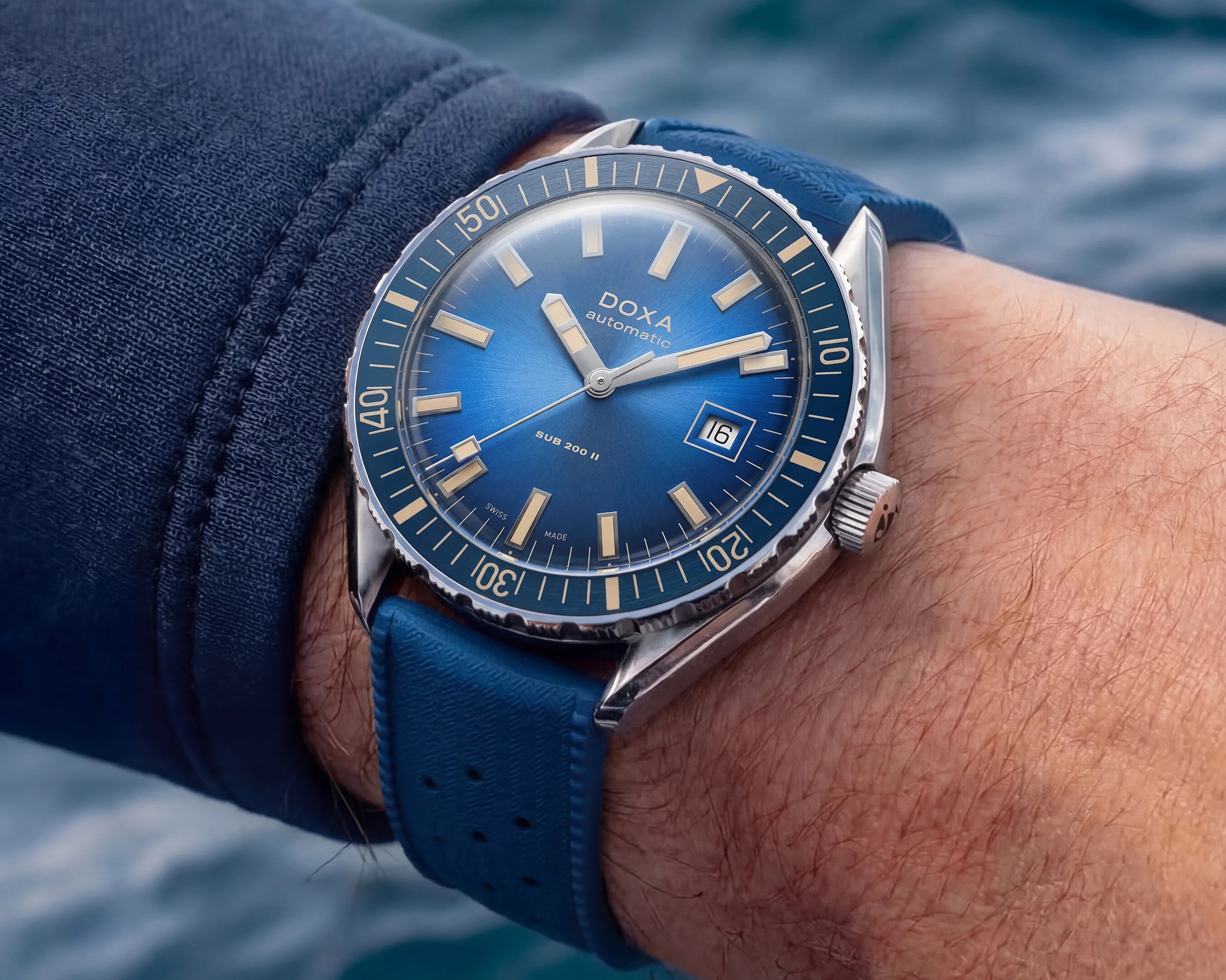 Blue Doxa Sub 200 II automatic wristwatch with beige markers and date window on a blue strap worn on a wrist.