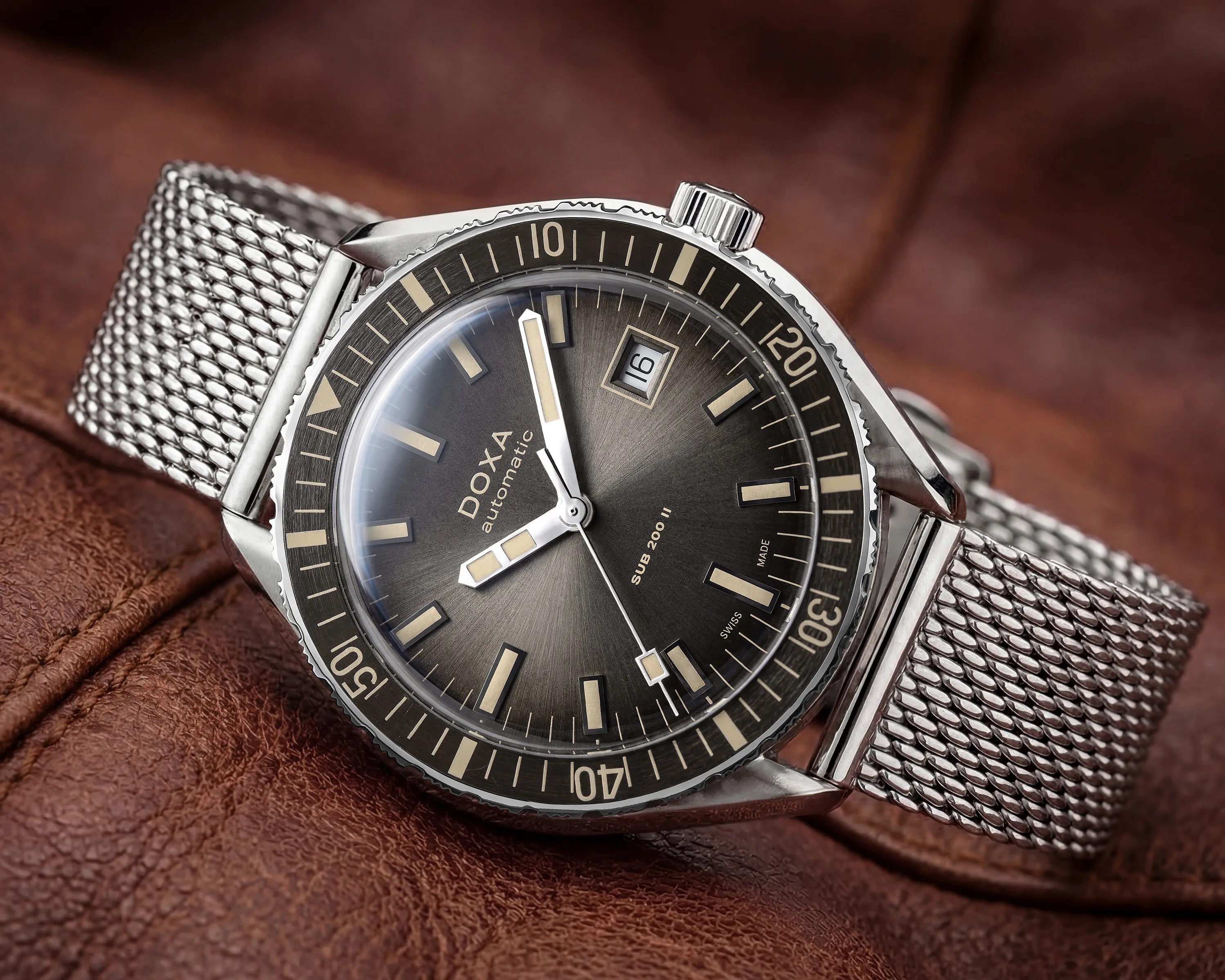 Silver Doxa Sub 200 II automatic watch with black dial and mesh bracelet on brown leather.