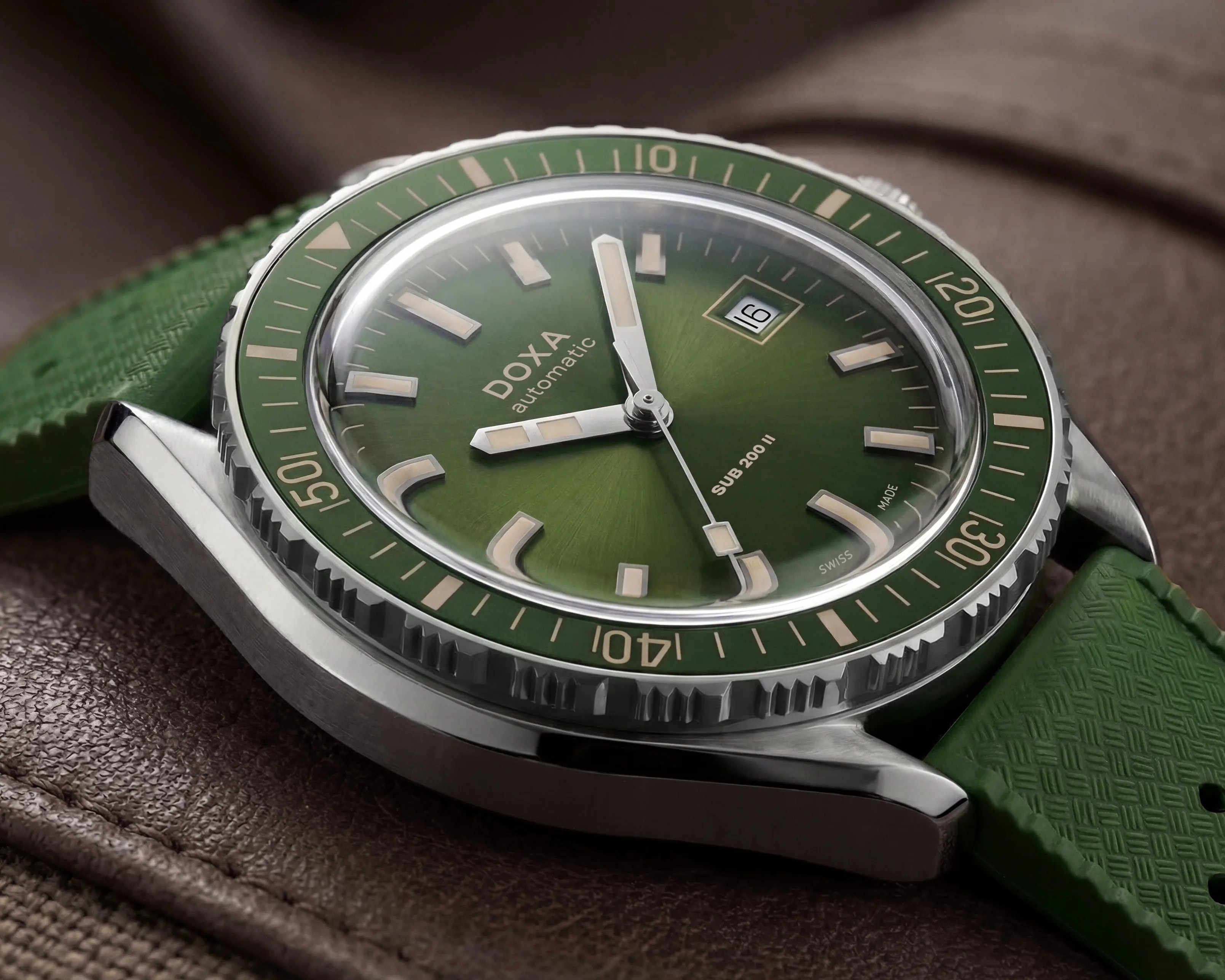 Green dial and bezel DOXA SUB 200 II automatic watch with date window and green textured strap on brown surface.