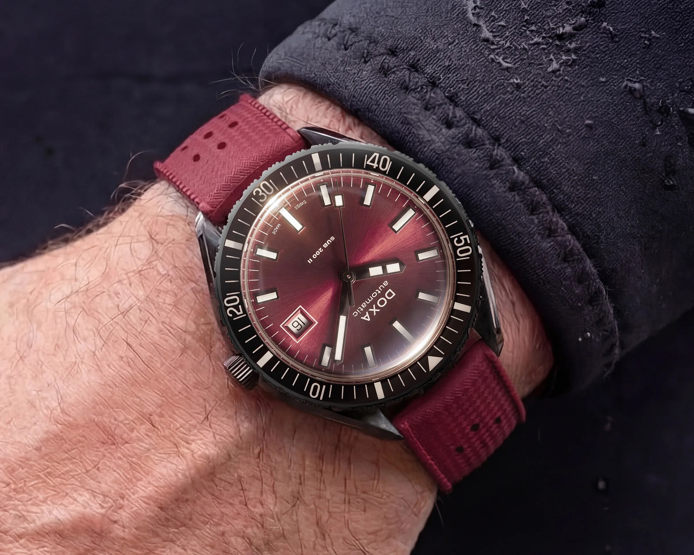 Wristwatch with a burgundy dial and matching fabric strap, black bezel with white markings, worn on a wrist.