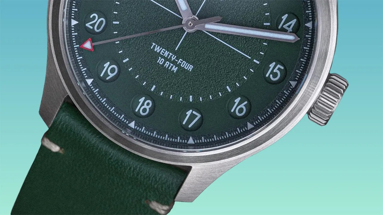 Close-up of a green dial wristwatch with a stainless steel case and green leather strap, showing 24-hour markings and a red-tipped second hand.