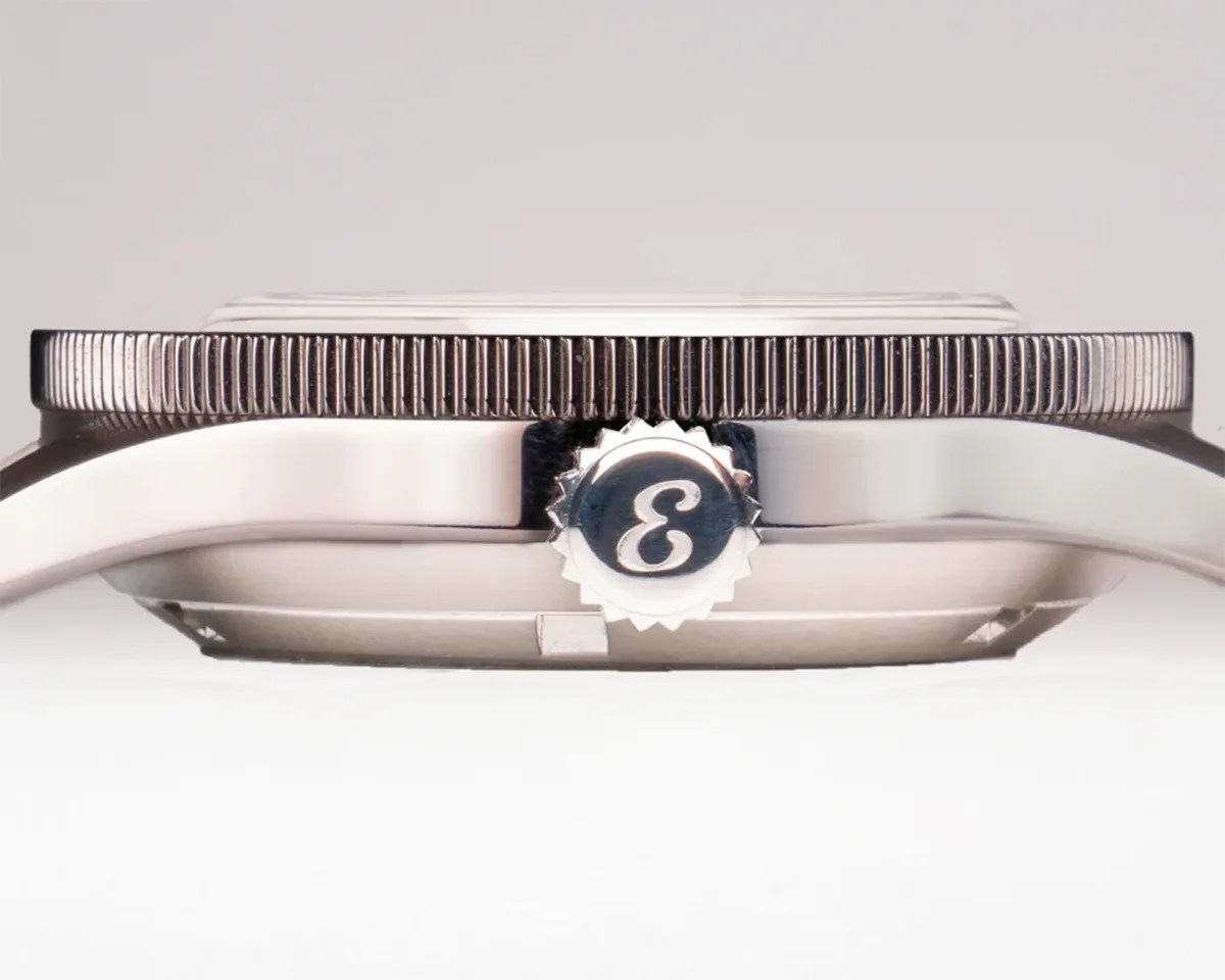 Close-up side view of a silver watch case with a ridged bezel and a crown featuring an engraved "3" logo.
