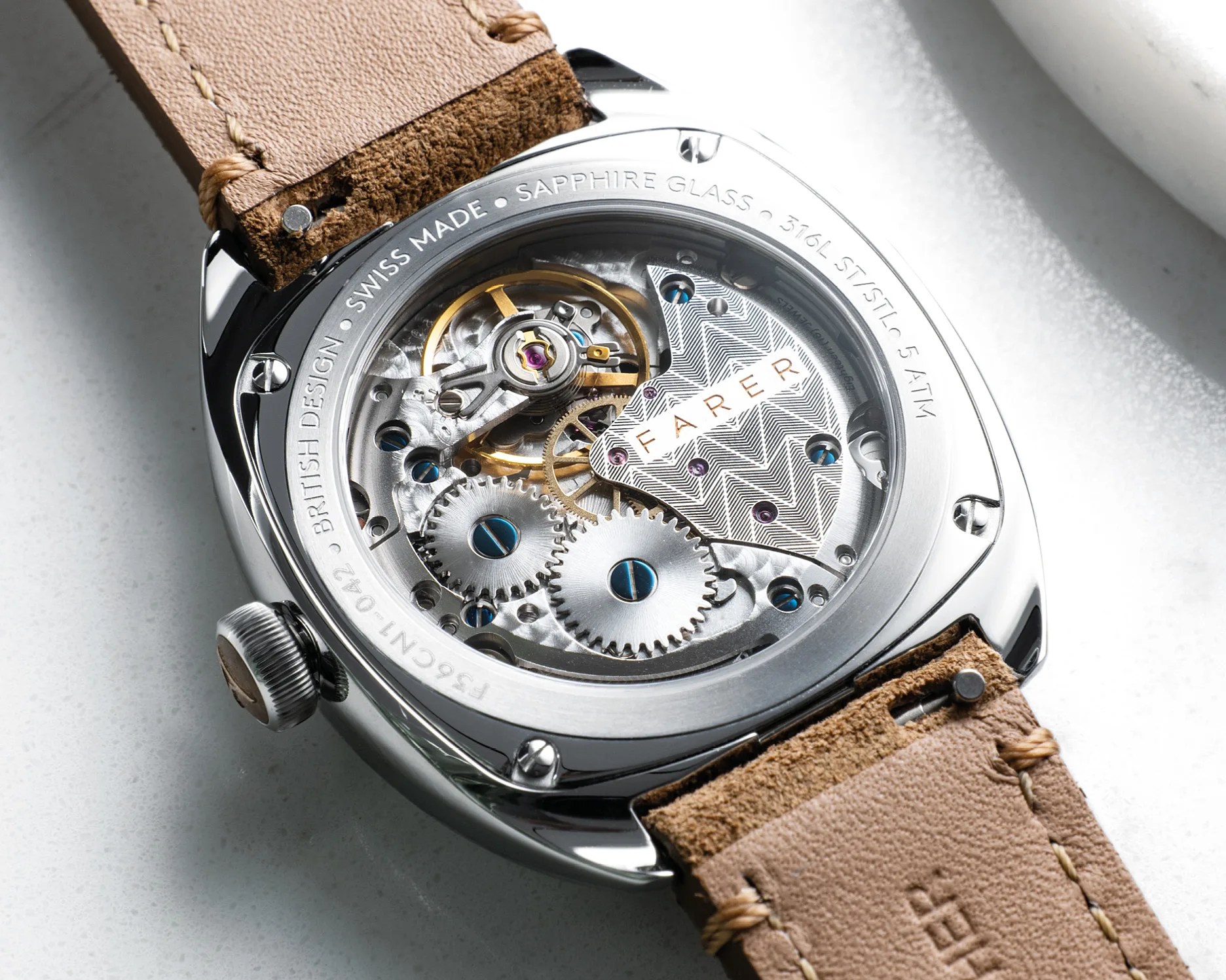 Close-up of the back of a Farer watch showing its mechanical movement with visible gears and a brown leather strap.