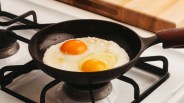 Cast iron skillet with two sunny-side-up eggs cooking on a gas stove burner.