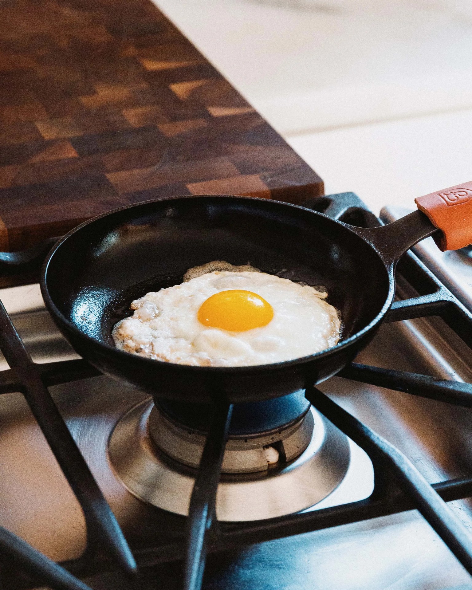 Black cast iron skillet with a leather handle cover frying a sunny-side-up egg on a gas stove.