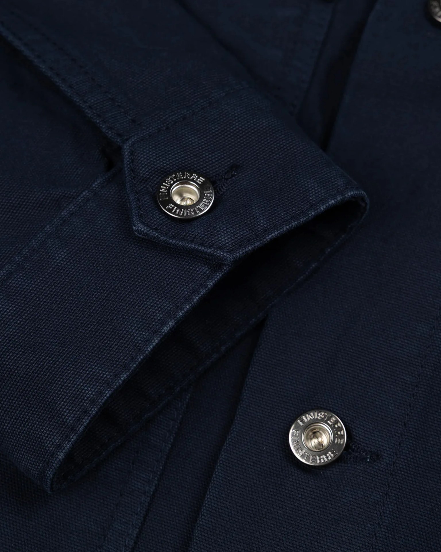 Close-up of navy blue fabric with silver snap buttons engraved with "Finisterre.