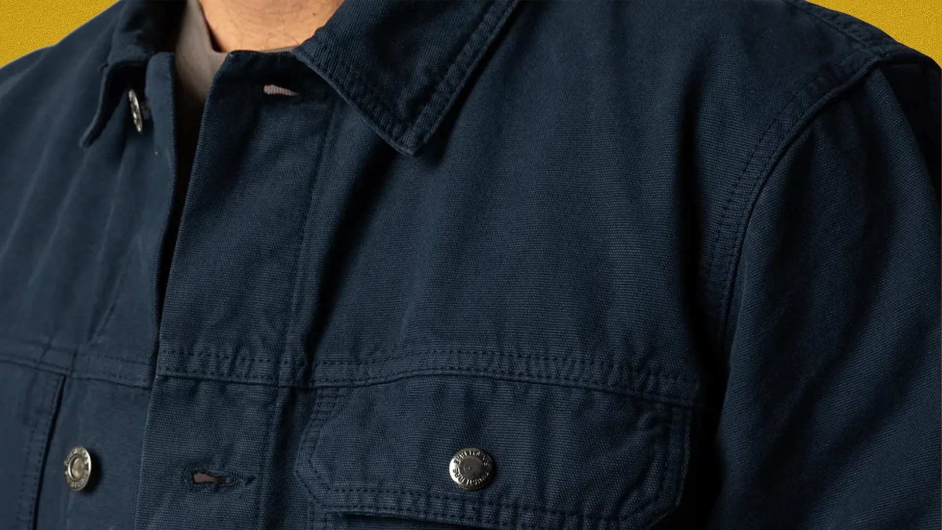 Close-up of a dark navy blue jacket with a collar and metal snap buttons on the chest pocket and front.