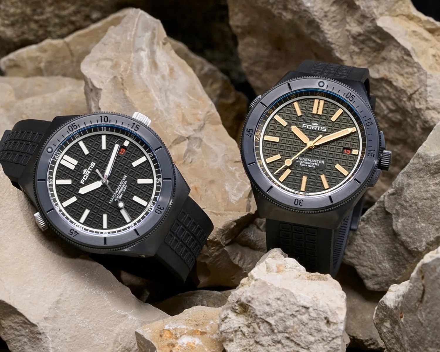 Two black Fortis Marinemaster wristwatches with textured dials and rubber straps resting on beige rocks.