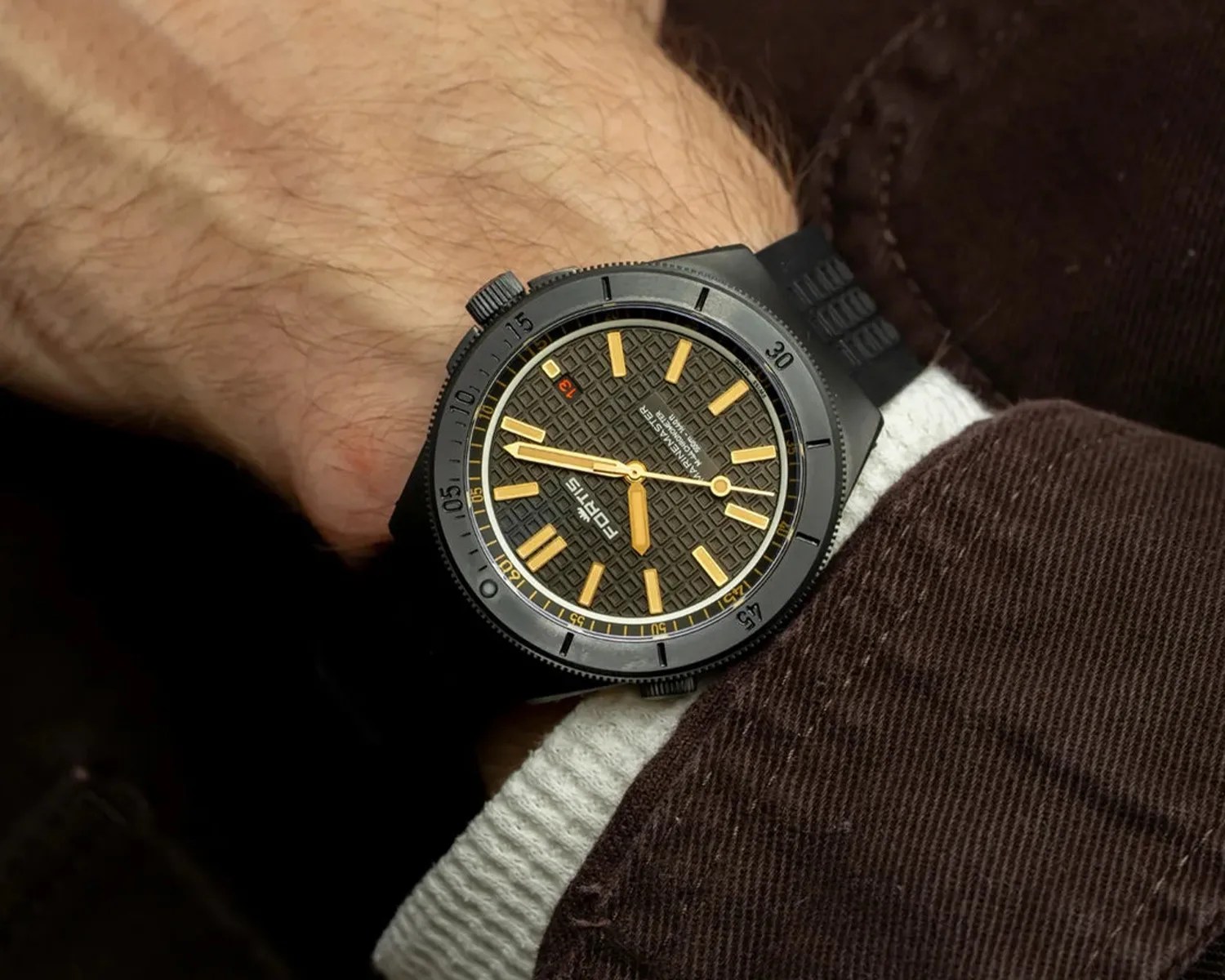 Black wristwatch with textured dial, gold hour markers and hands, and black rubber strap worn on a wrist.