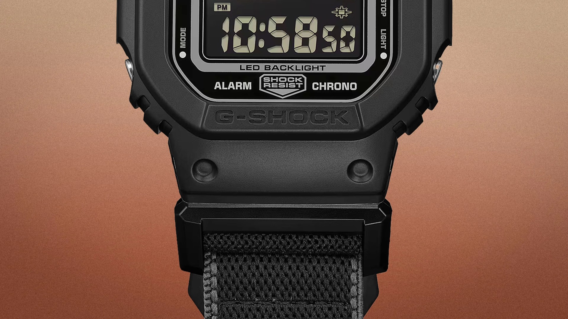 Close-up of a black G-Shock digital watch with LED backlight and black fabric strap against a gradient brown background.