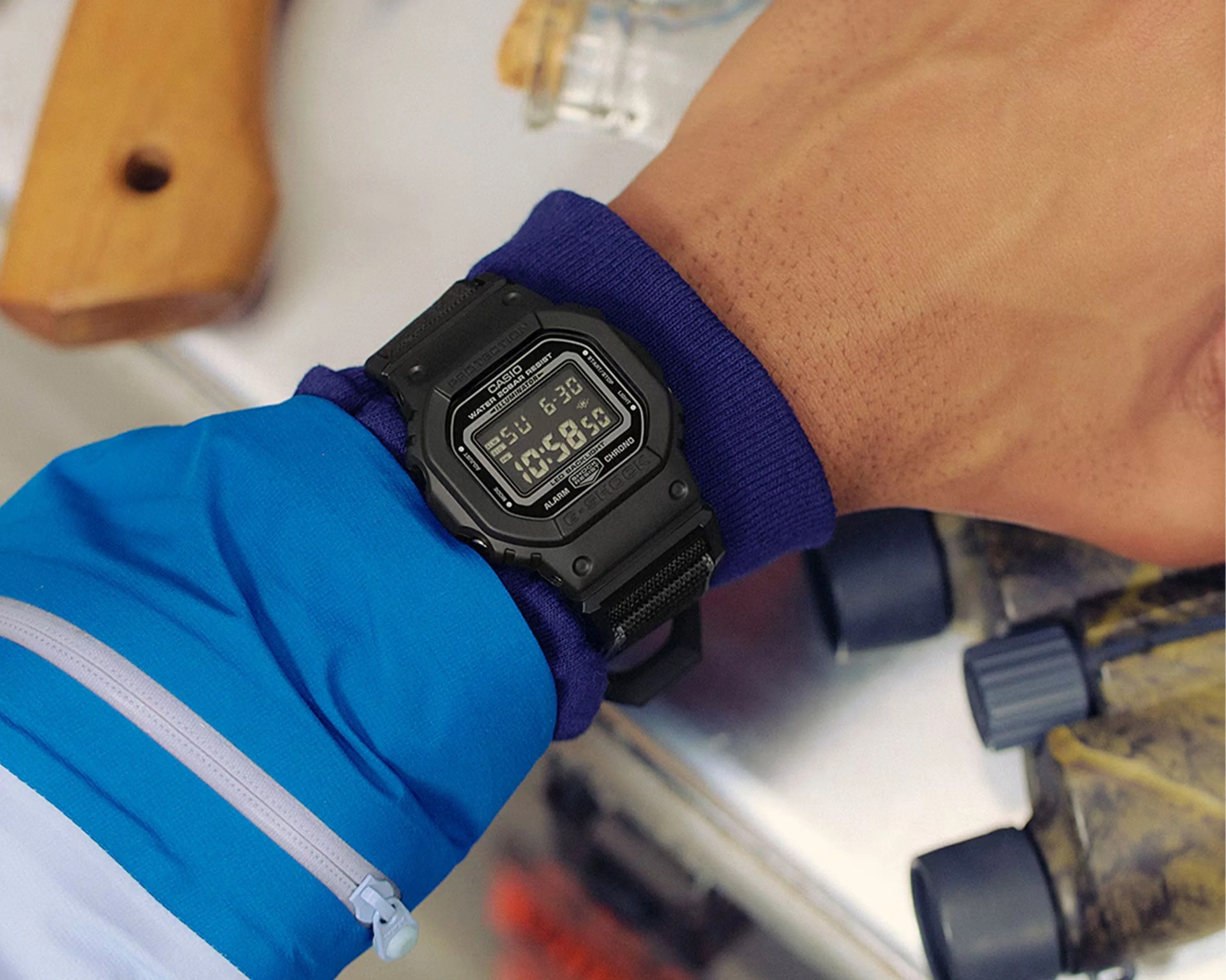 Black Casio G-Shock digital watch with fabric strap worn over a blue and purple jacket sleeve.