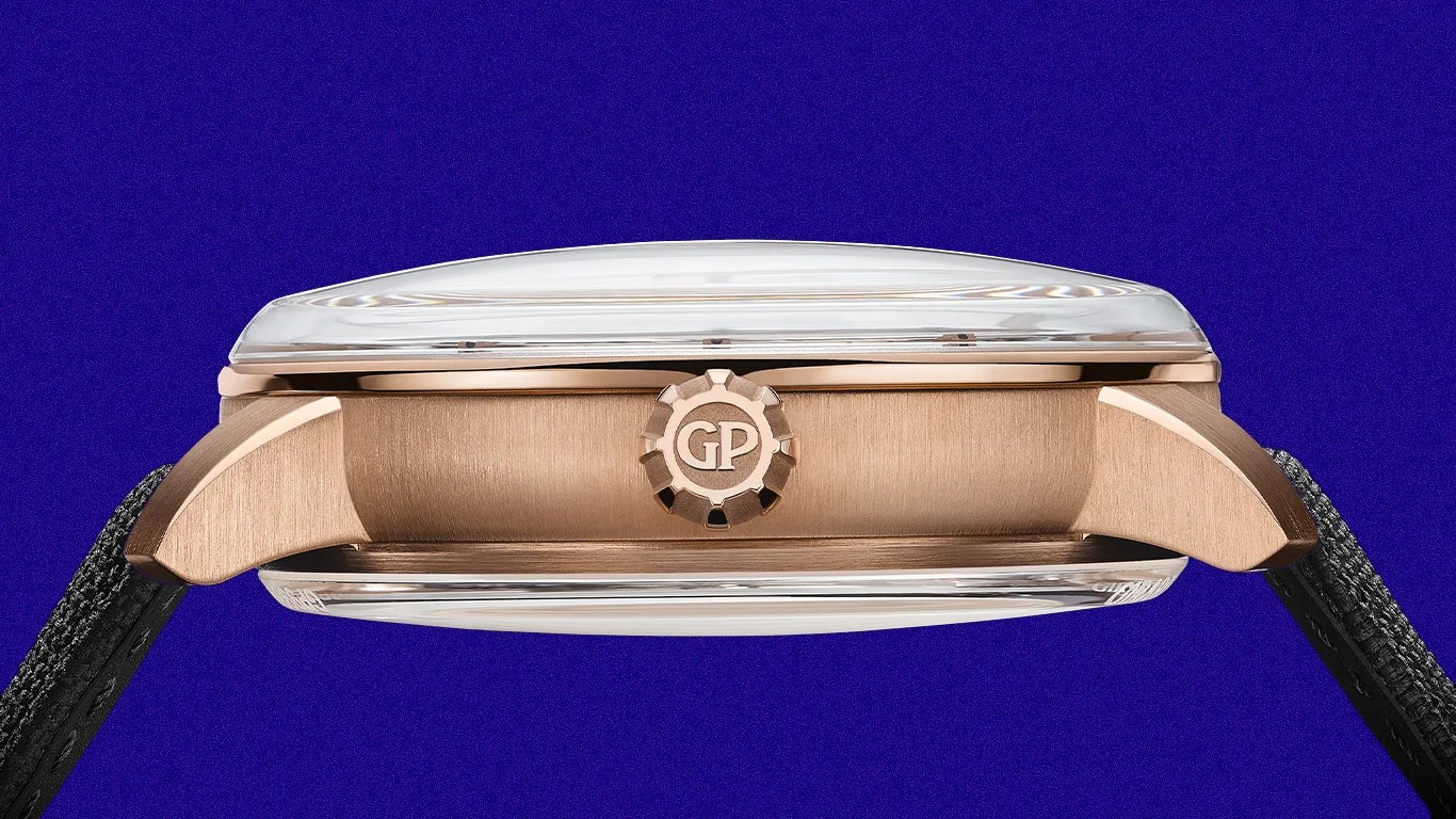 Side view of a rose gold watch case with a domed crystal and a black textured strap.
