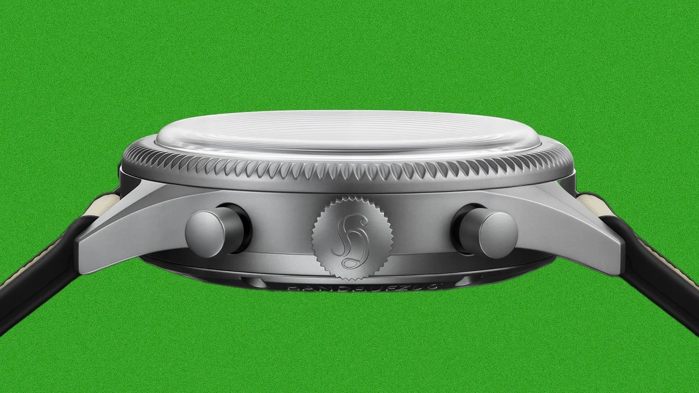 Side view of a silver watch case with two pushers and a crown engraved with a stylized "S" logo, attached to a black strap.