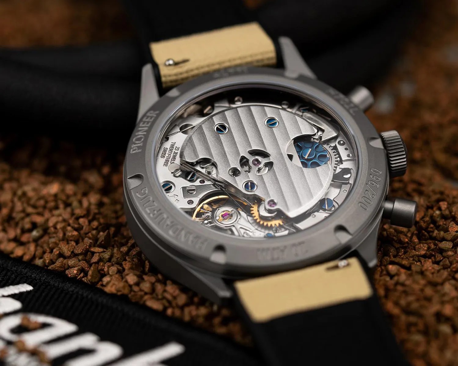 Close-up of the back of a mechanical wristwatch showing intricate silver and blue gears with a beige and black strap.