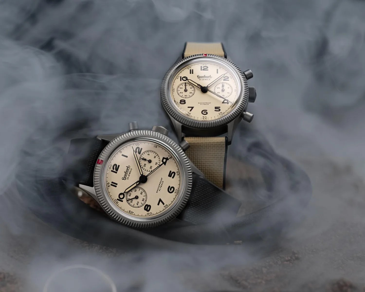 Two vintage-style wristwatches with beige dials and black numerals, one with a beige strap and one with a black strap, surrounded by smoke.