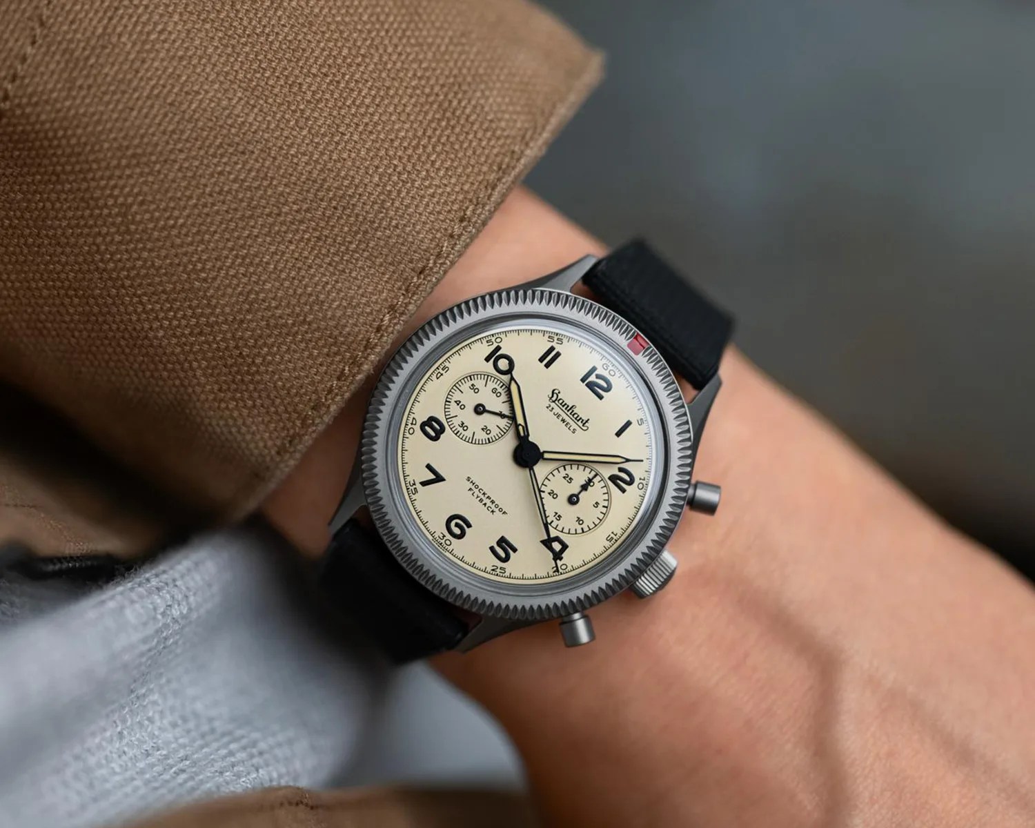 Wristwatch with cream dial, black numerals, two subdials, and black strap worn on a wrist.