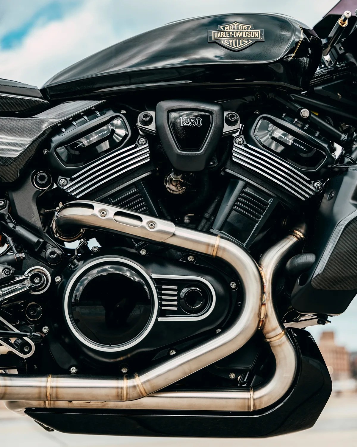 Close-up of a black Harley-Davidson motorcycle engine with "1250" on the air filter cover and silver exhaust pipes.