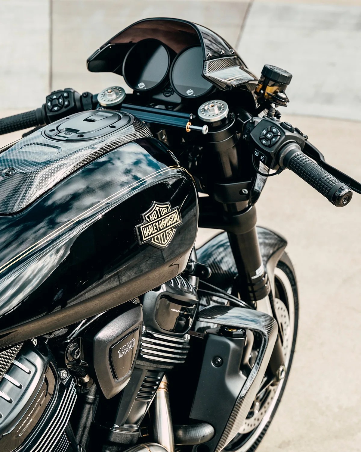 Glossy black Harley-Davidson motorcycle fuel tank with carbon fiber accents and detailed handlebars.