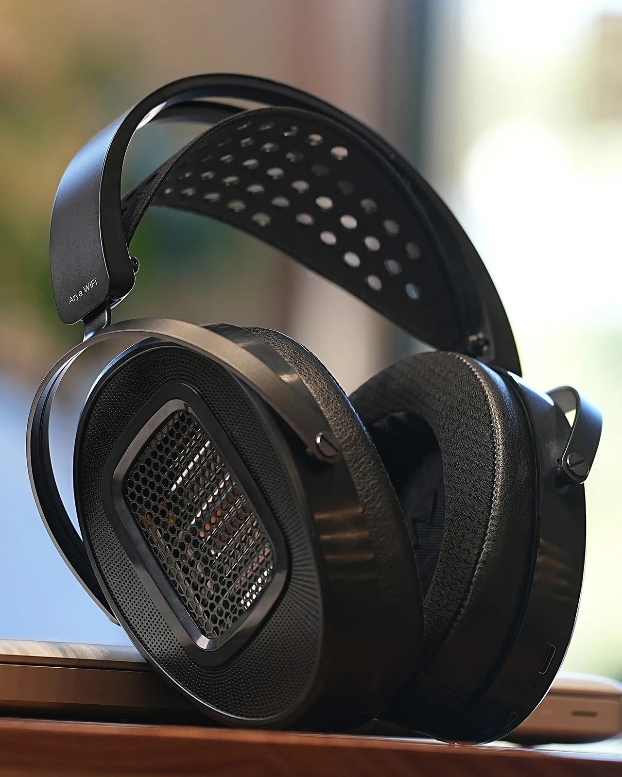 Black over-ear headphones with perforated headband and mesh ear cups resting on a wooden surface.