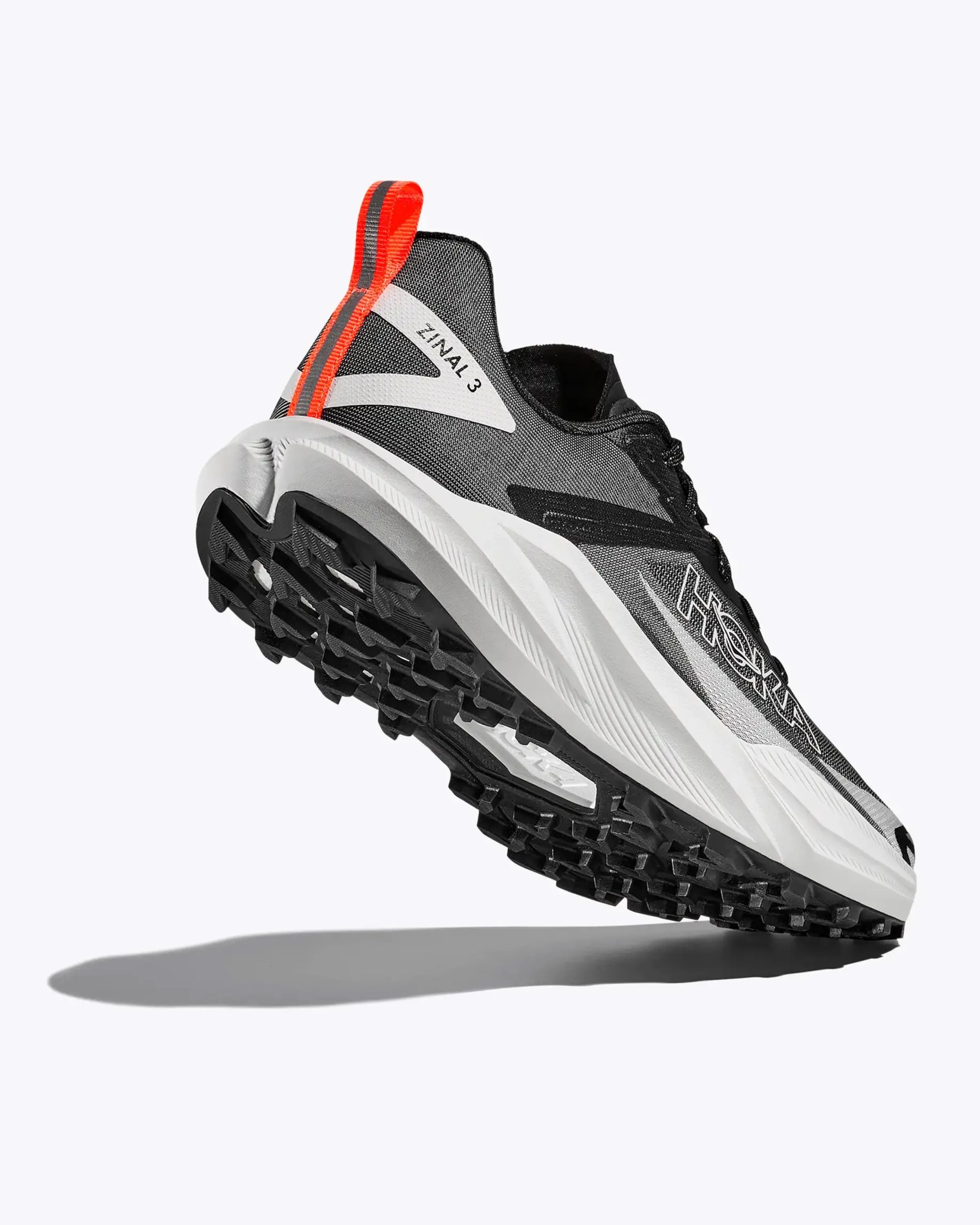 Black and white Hoka Zinal 3 running shoe with orange pull tab and rugged black sole.