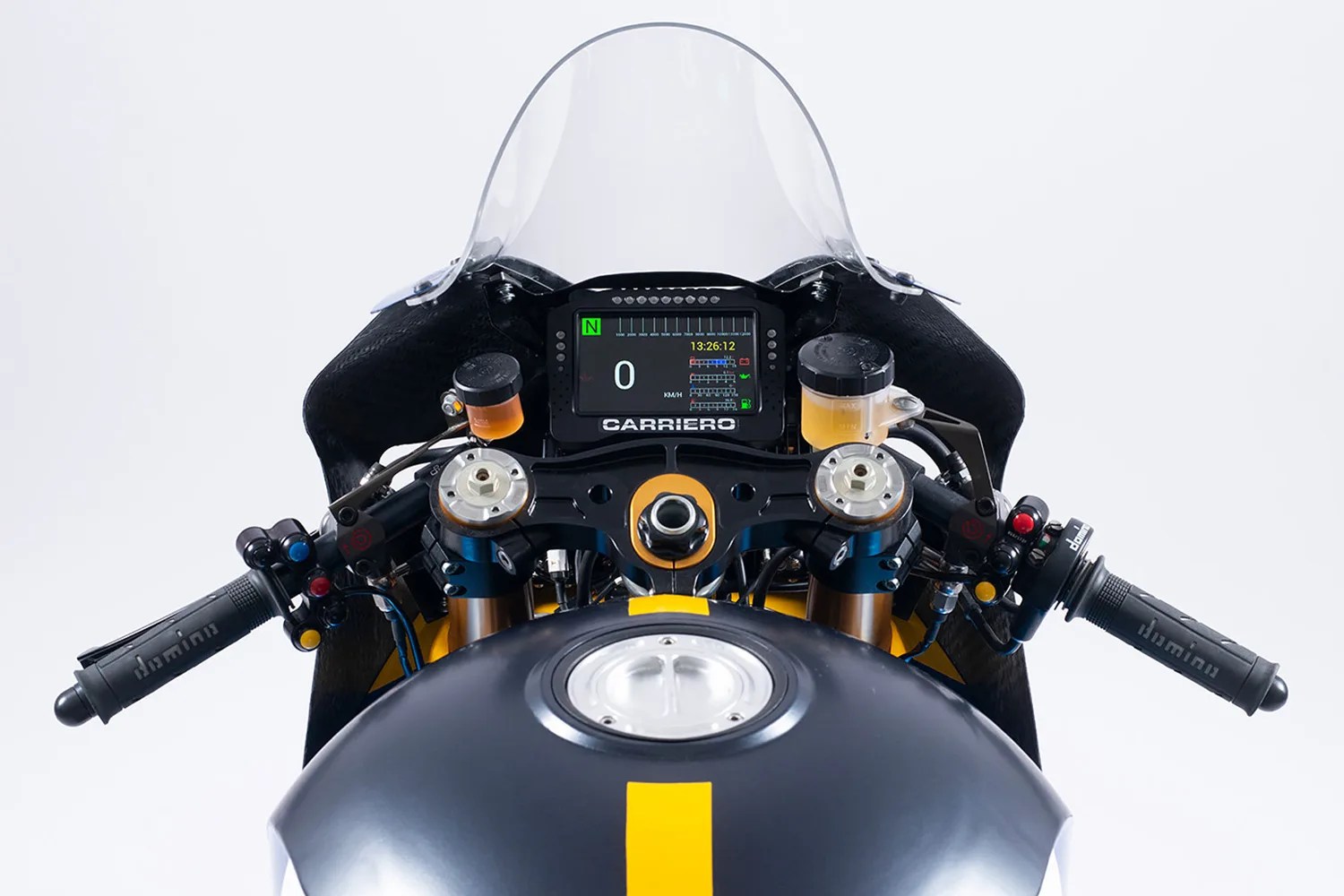 Motorcycle cockpit view showing black and yellow fuel tank, digital dashboard with "CARRIERO" label, and black handlebars with controls.