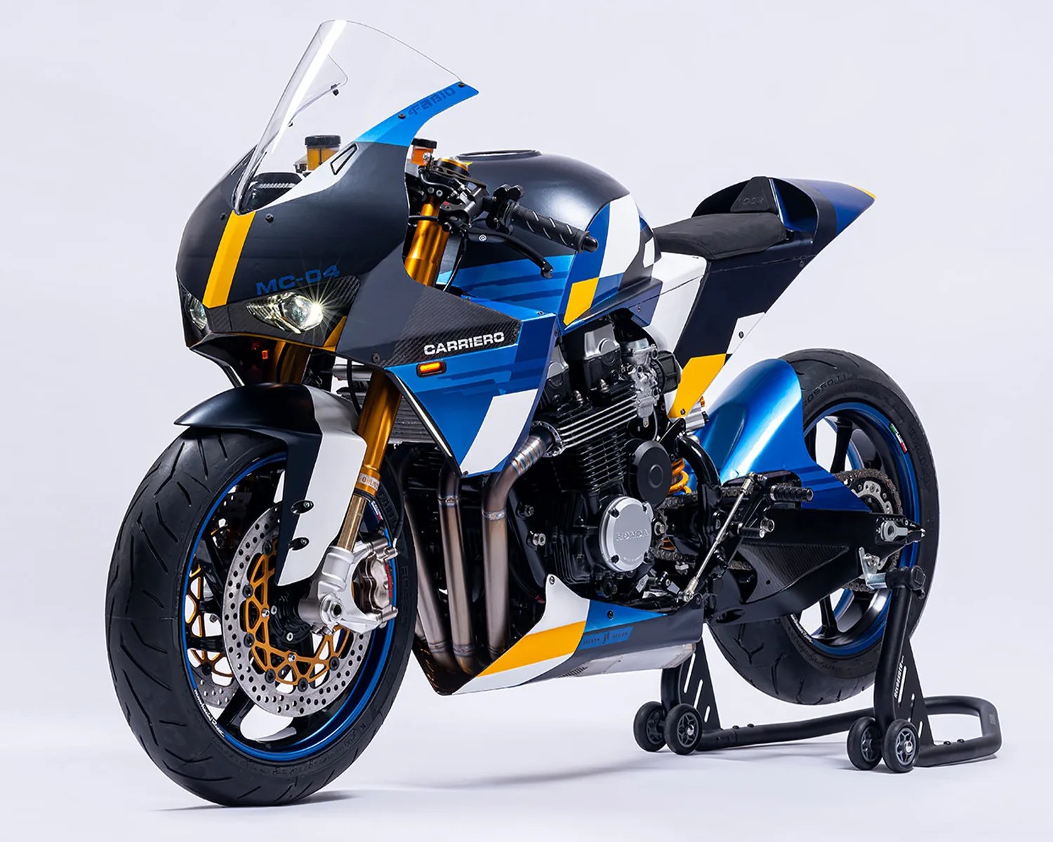 Blue, black, white, and yellow sport motorcycle with gold front forks on a rear stand.