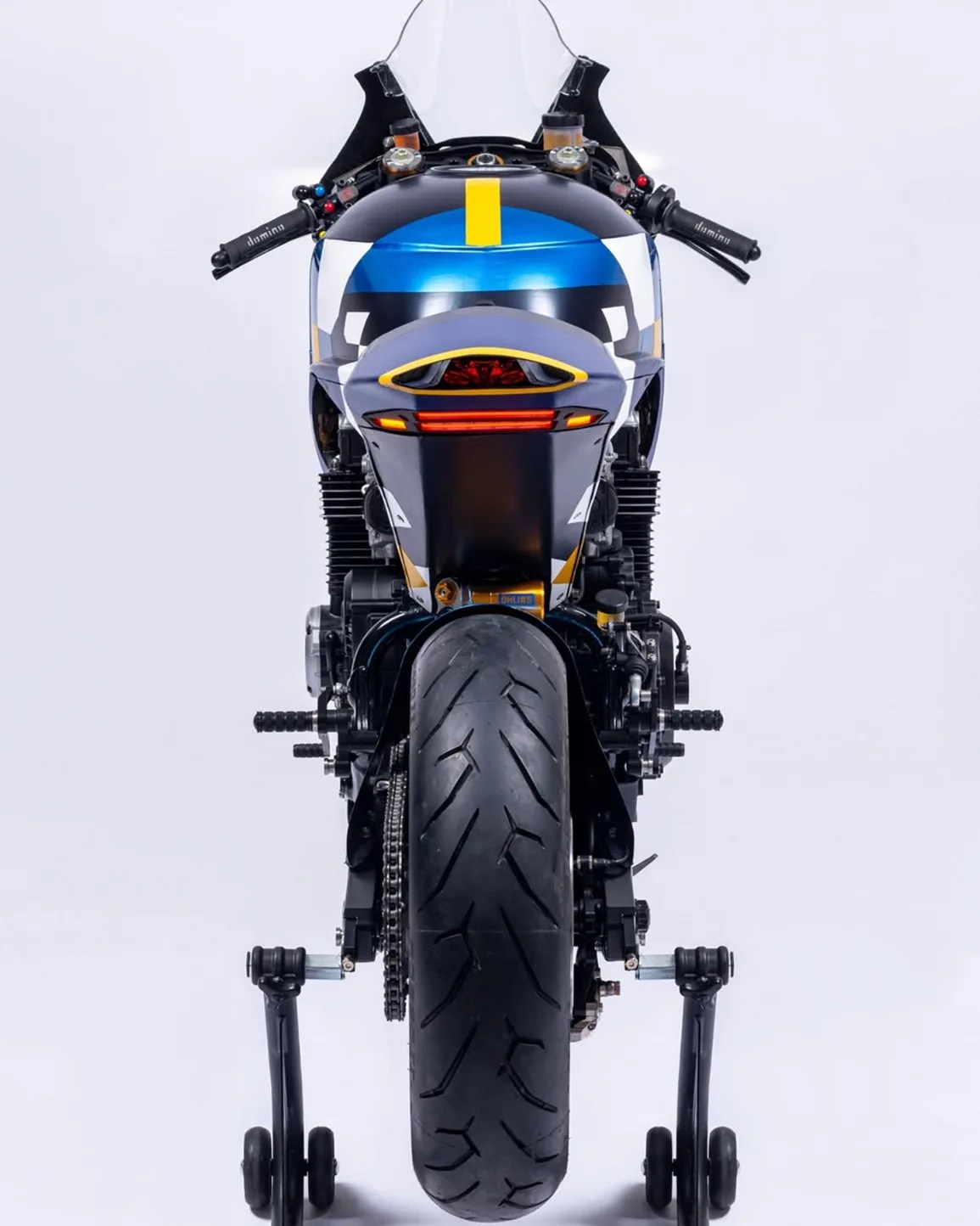 Rear view of a black and blue sport motorcycle with yellow accents on a rear stand against a white background.