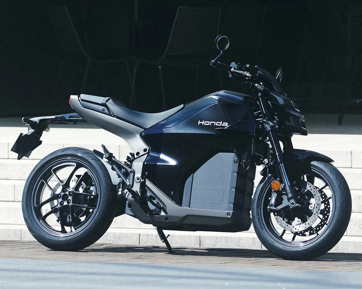 Black Honda electric motorcycle parked on pavement with steps in the background.