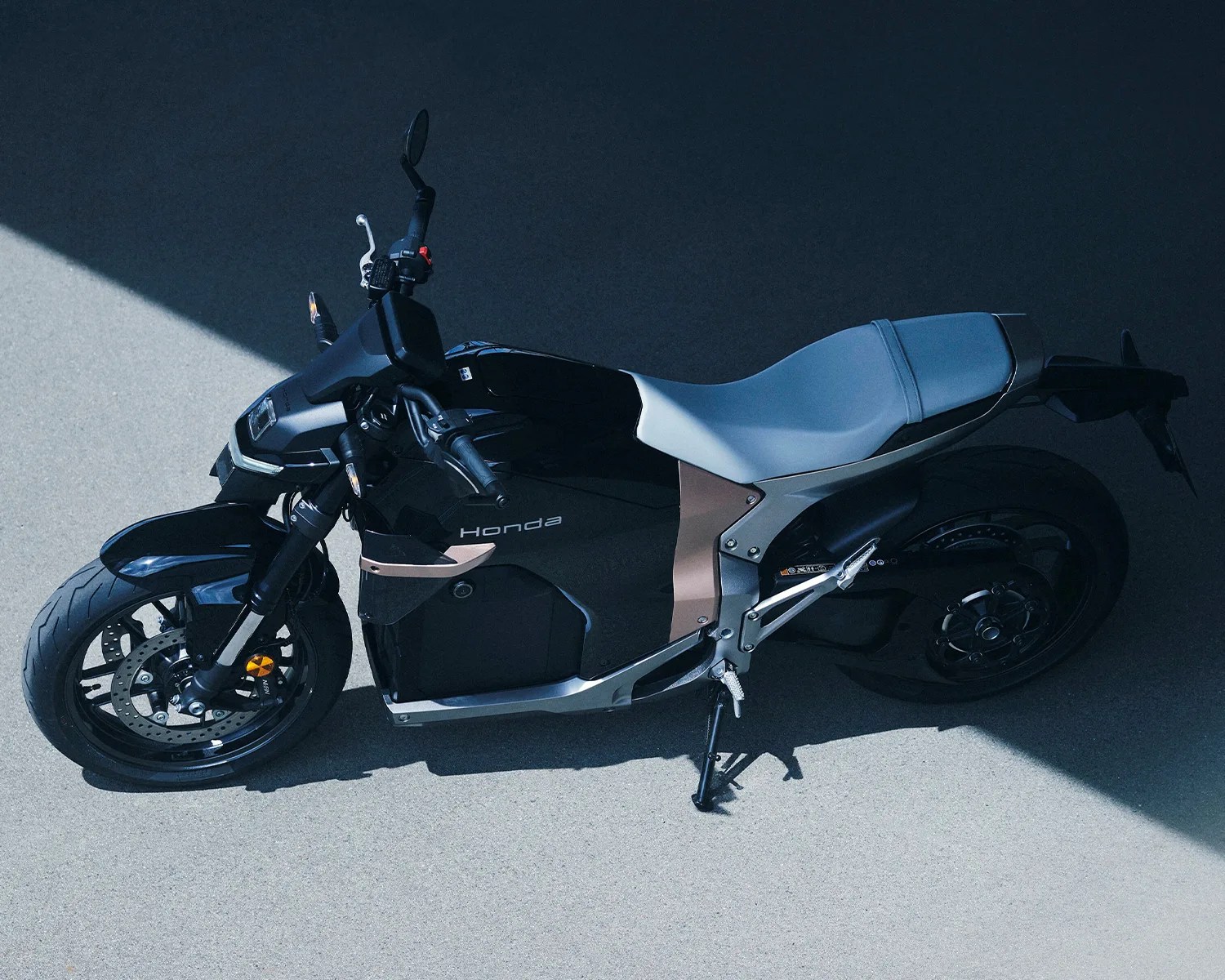 Black Honda electric motorcycle with gray seat parked on a concrete surface partially in sunlight.