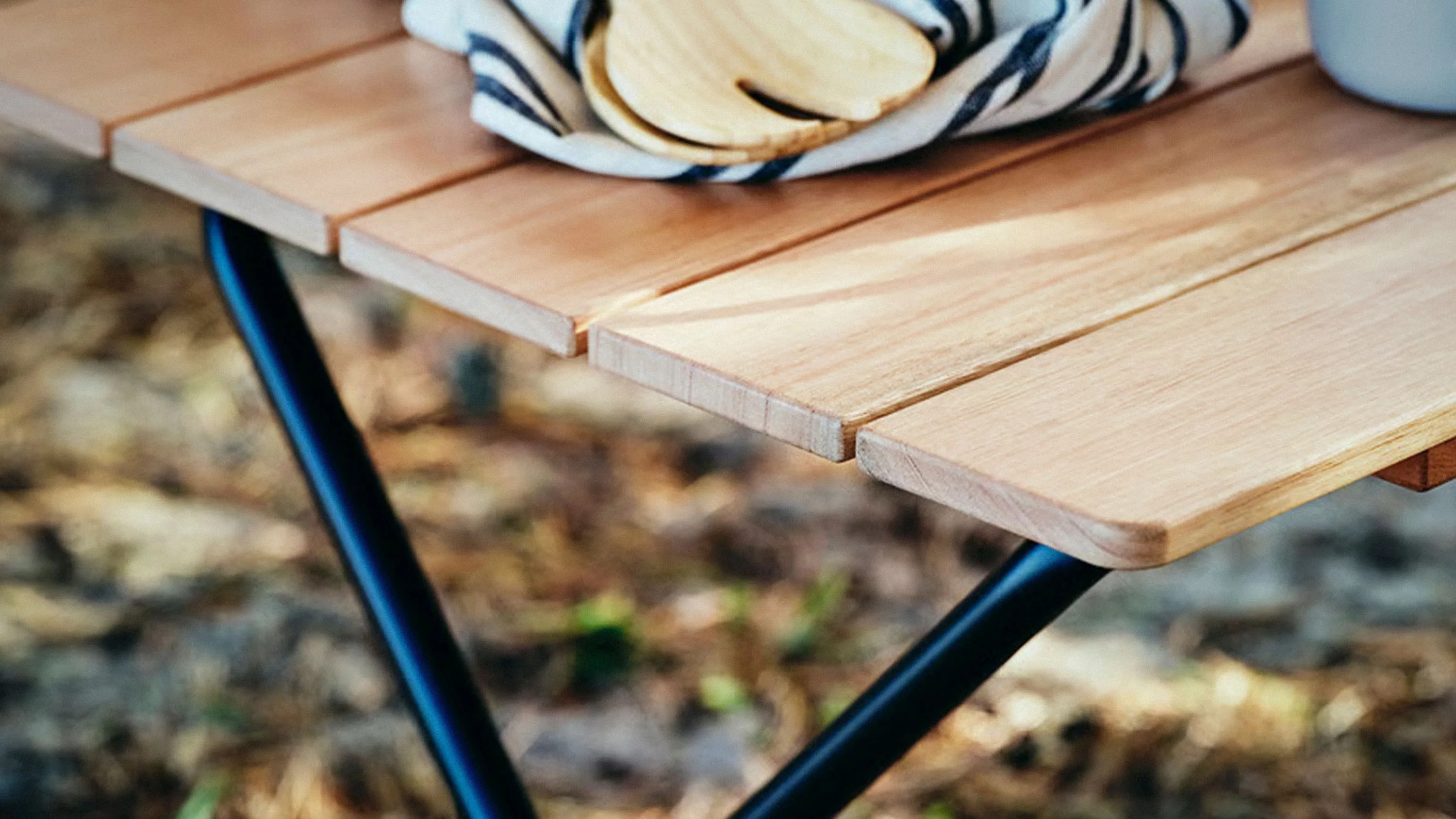 Close-up of a light wooden slatted table top with black metal legs outdoors.