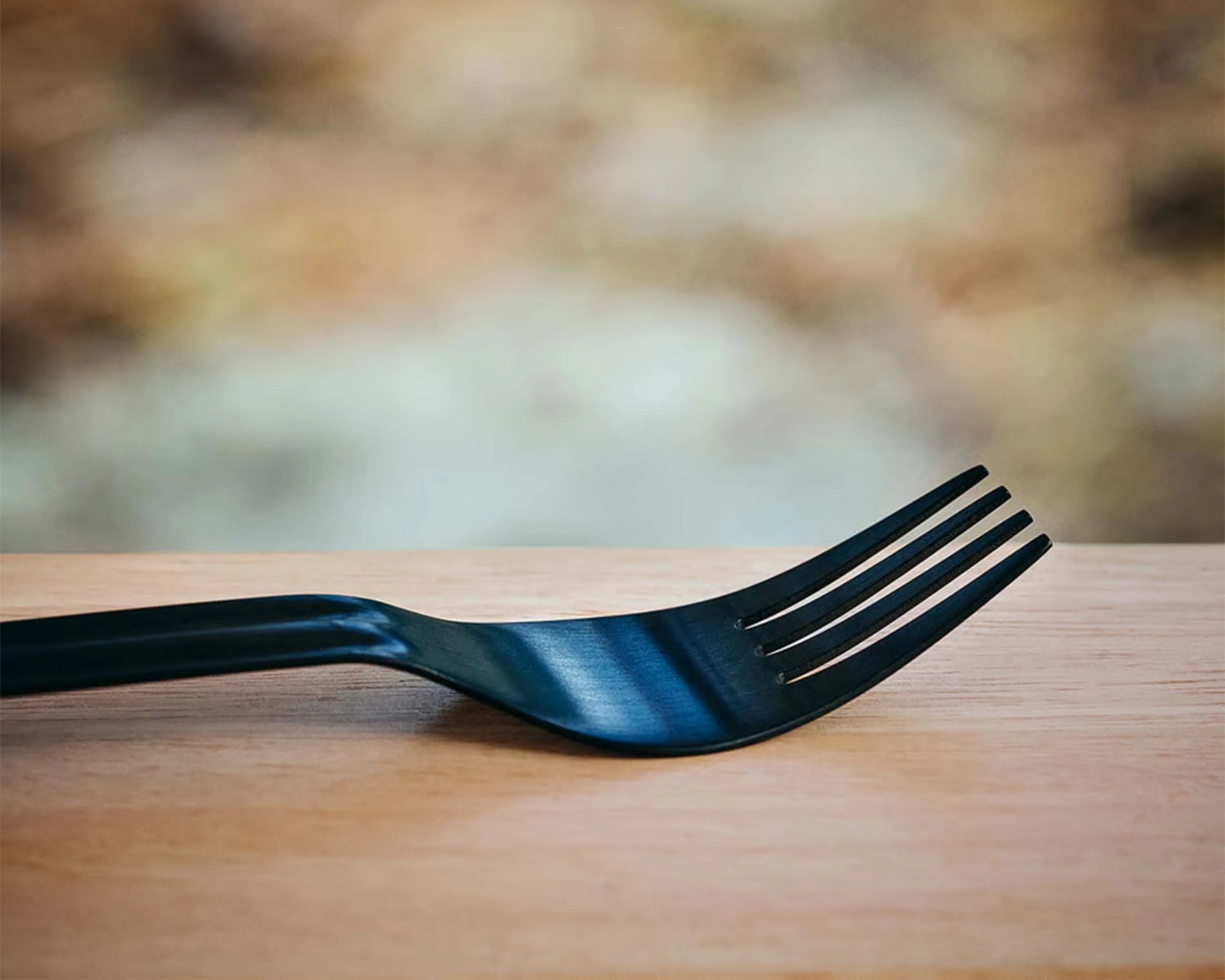 Black plastic fork resting on a wooden surface with a blurred background.