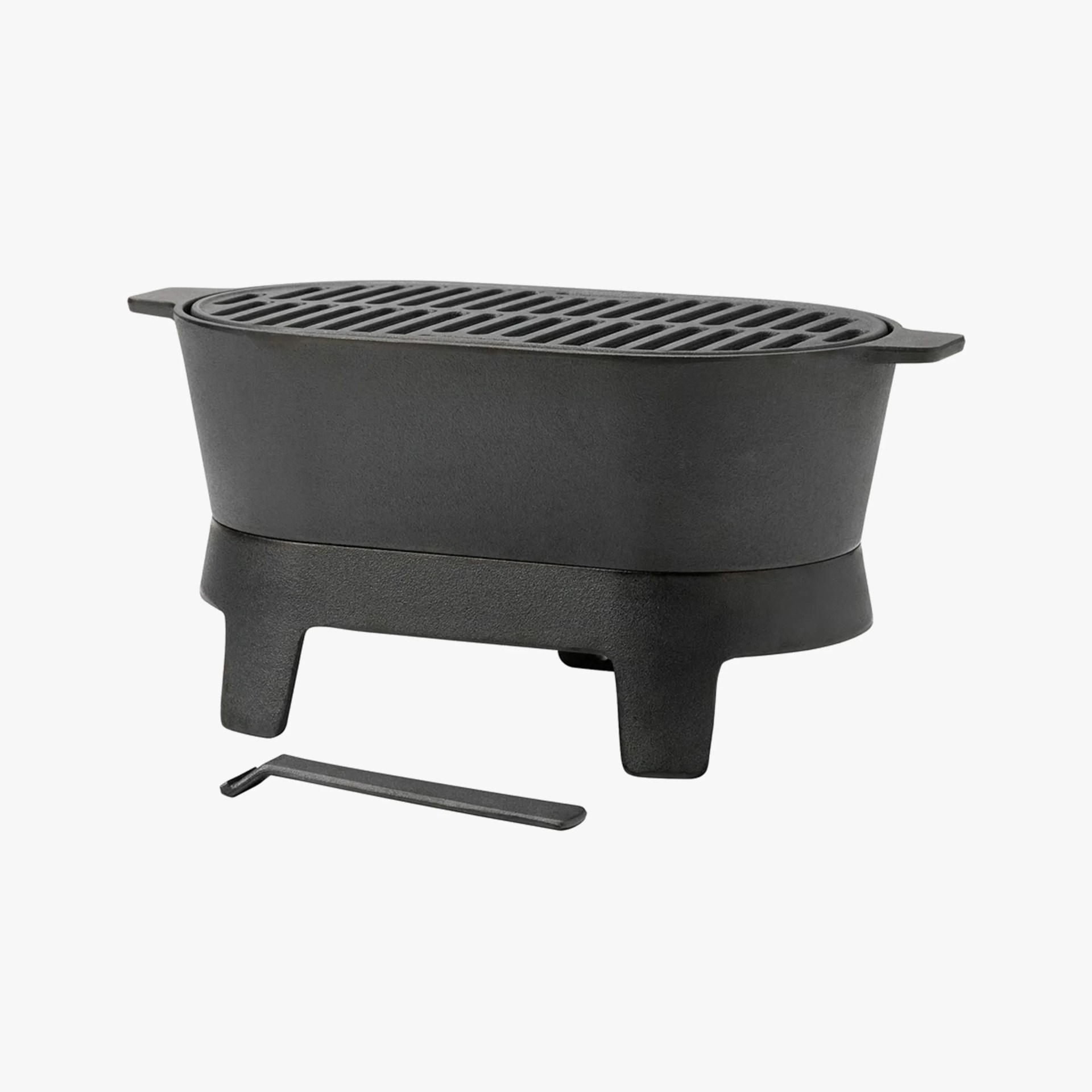 Black cast iron tabletop grill with legs and a small metal tool beside it.