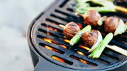 Grilled meatballs and green onions on wooden skewers over a hot charcoal grill.