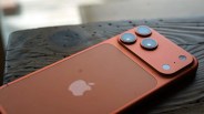 Copper-colored iPhone with triple camera lenses on a dark wooden surface.