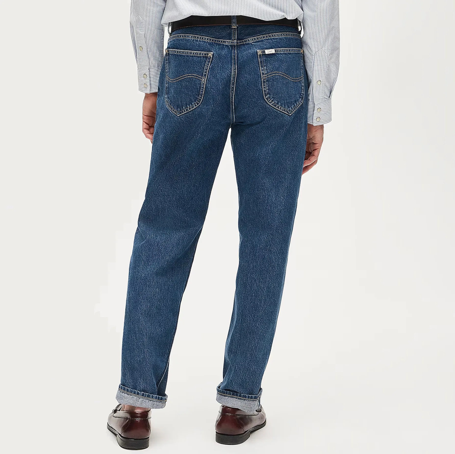 Back view of dark blue straight-leg jeans with rolled cuffs worn with brown leather shoes and a striped shirt.