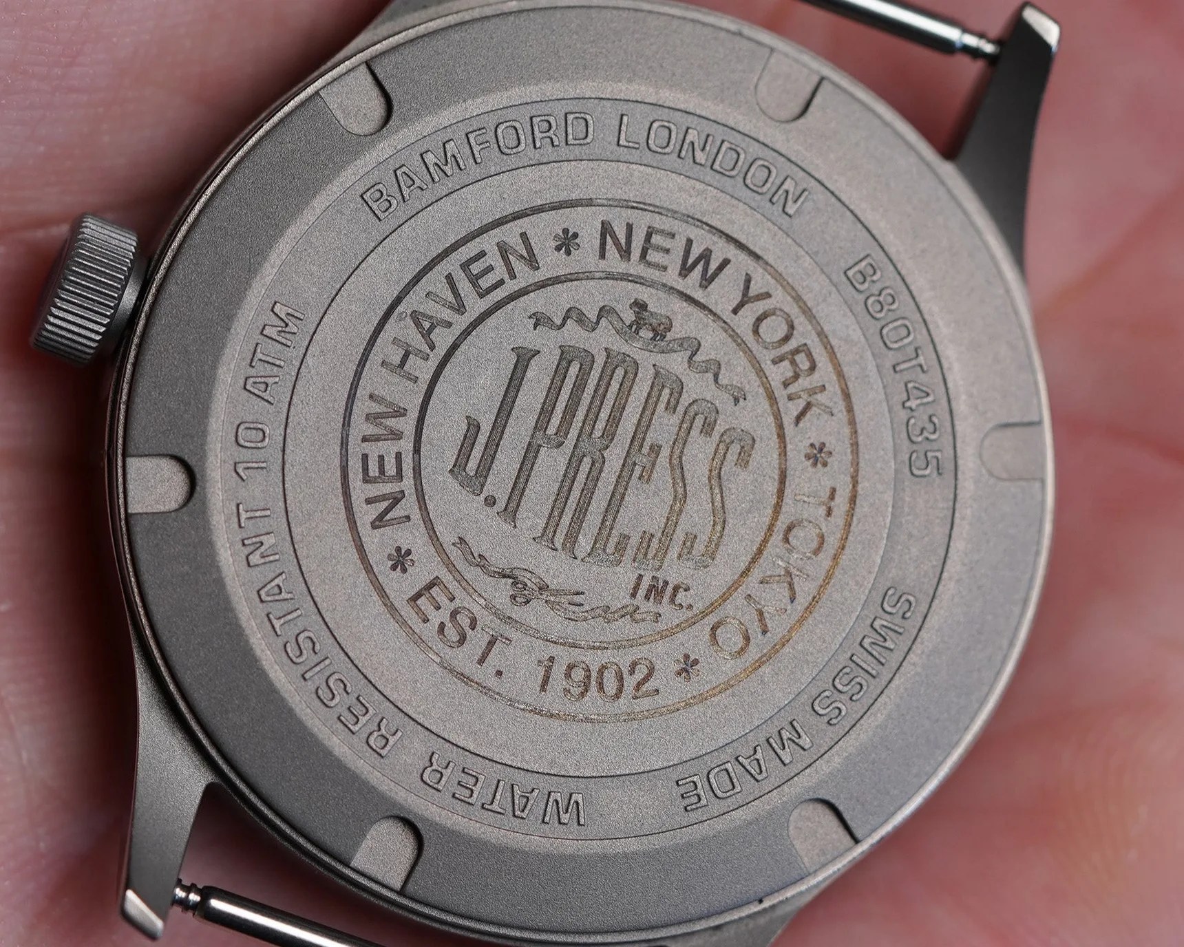 Matte gray watch back engraved with "J. Press Inc.," "Bamford London," "Swiss Made," and water resistance details.
